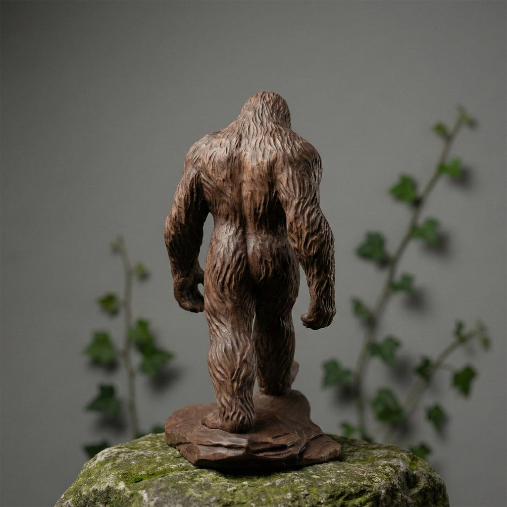 Statue of a wooden bigfoot creature on a rock with a blurred plant background